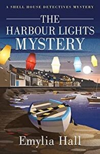 book cover for The Harbour Lights Mystery by Emylia Hall. A vector shows a harbour scene with lantern lights strung across the top of the cover