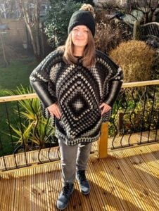 A woman is standing on a decking wearing a crochet poncho