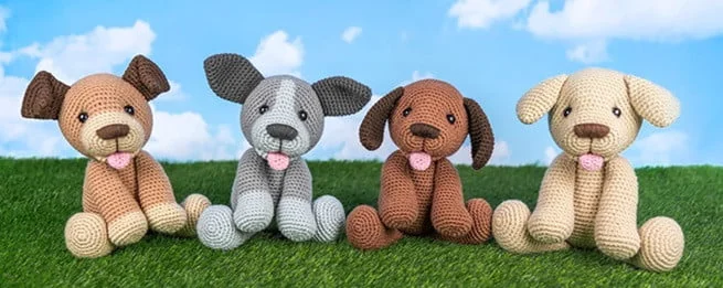 four crocheted puppies are sitting on grass in a line