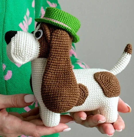 A person is holding out two hands holding a Bassett Hound