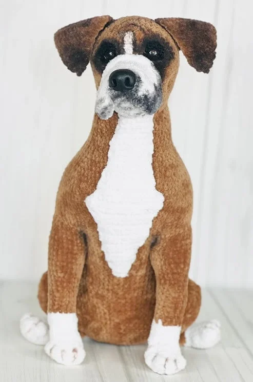 A crocheted Boxer dog is sitting upright on the floor