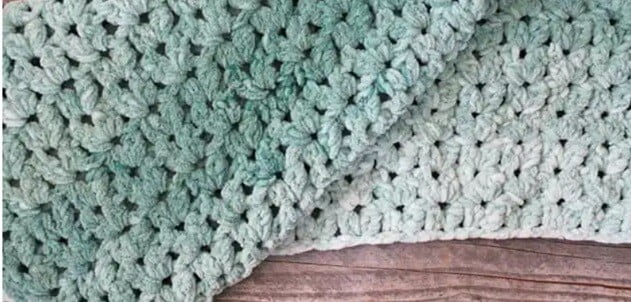A blanket crocheted in bulky yarn is folded on the floor