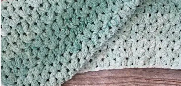 A blanket crocheted in bulky yarn is folded on the floor