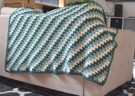 A blanket crocheted in green is draped along the back of a settee