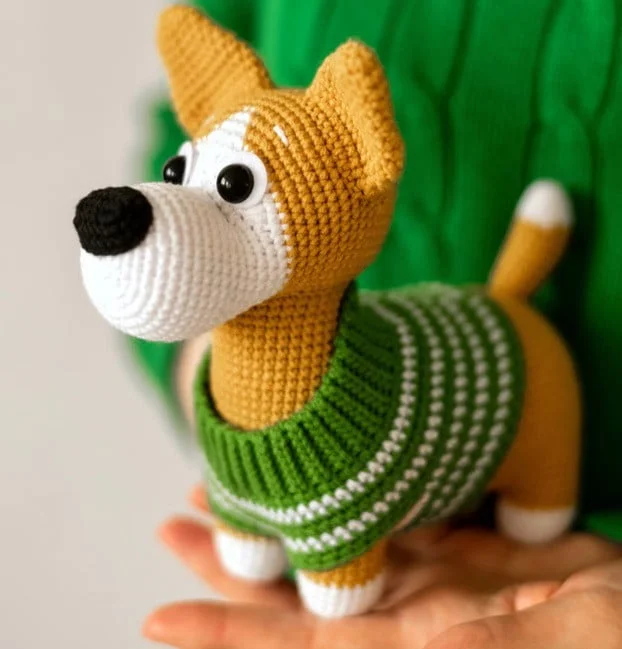 A child has both hands out with a crochet Corgi in their hands