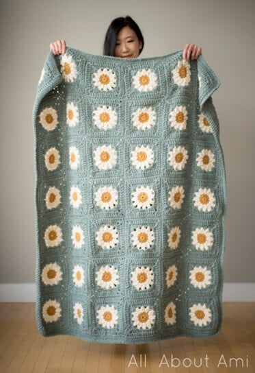 A woman is holding up a blanket crocheted in daisy granny squares