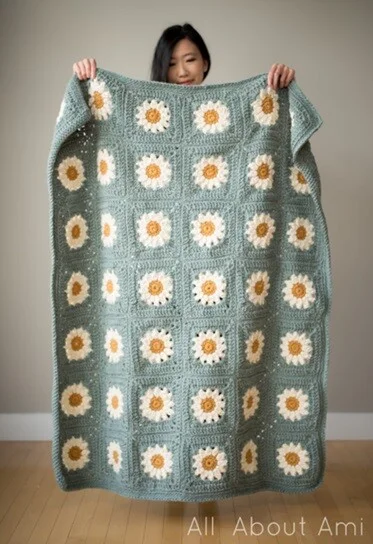 A woman is holding up a blanket crocheted in daisy granny squares