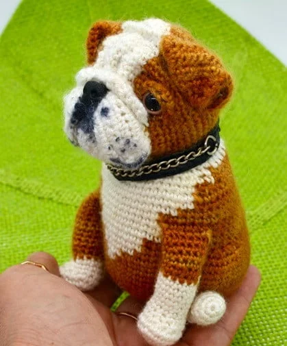 A toy English Bulldog is being held in a hand