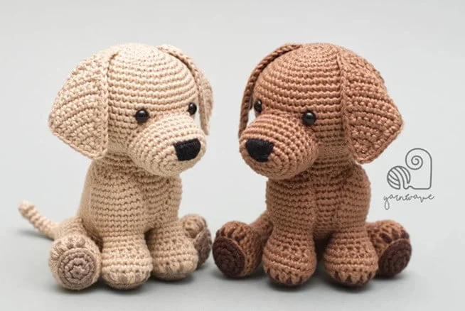 2 crochet dogs in cream and brown are facing each other