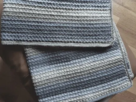 A blanket crocheted in shades of grey is folded on the floor