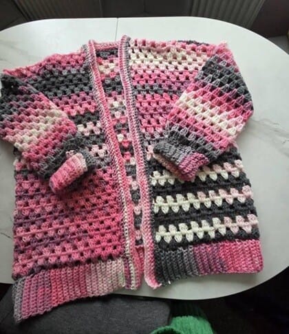 granny stitch cardigan crocheted in variegated yarn (pink, black and grey) is laid out flat