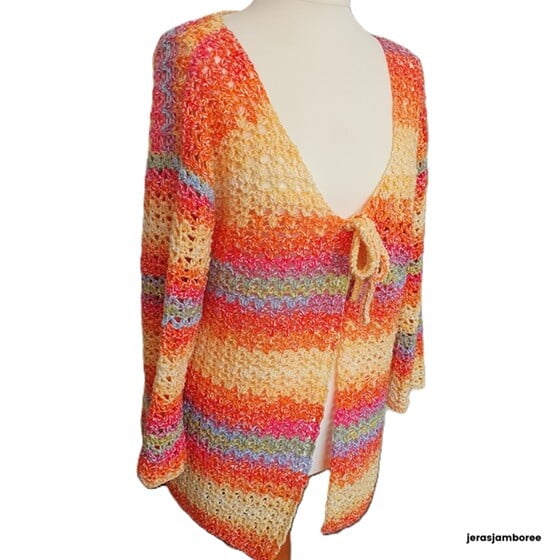 A crochet cardigan in orange, yellow, purple, green and blue is styled on a mannequin