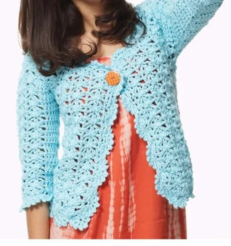 Woman wearing a sky blue crochet summer cardigan with scalloped edges, three-quarter sleeves, and a single orange button closure, layered over a coral tie-dye dress.