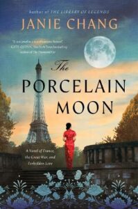 book cover for The Porcelain Moon by Janie Chang. A woman in a red dress is standing in front of a French landmark with a full moon hanging in the sky