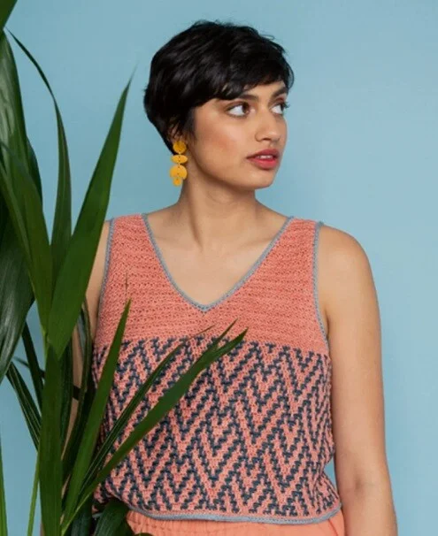 A woman is standing behind a leafy shrub wearing a crochet top
