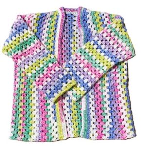 A granny stitch cardigan crocheted in bright colours is laid out flat with the arms folded over