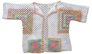 A hexagon crochet cardigan in white and bright rainbow colours is laid out flat