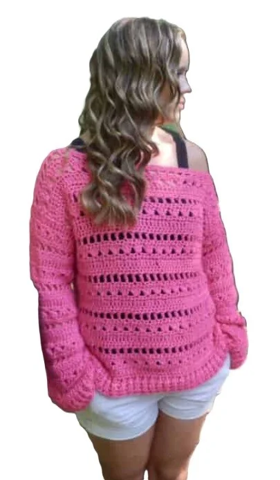 Woman wearing a bright pink off-the-shoulder crochet sweater with a mix of solid and openwork stitch rows. The sweater has a relaxed fit with long sleeves and is paired with white shorts, shown against a white background.