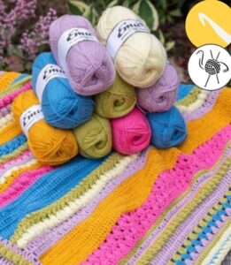 crocheted blanket laid flat with 9 balls of yarn placed in a pyramid on top of the blanket