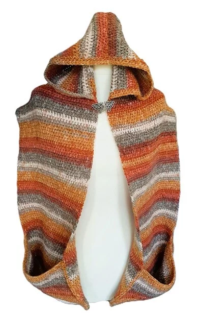 A crochet hooded pocket scarf is styled on a mannequin showing the front view with the hood up