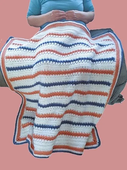 A woman is sat on a sofa with a blanket over her lap