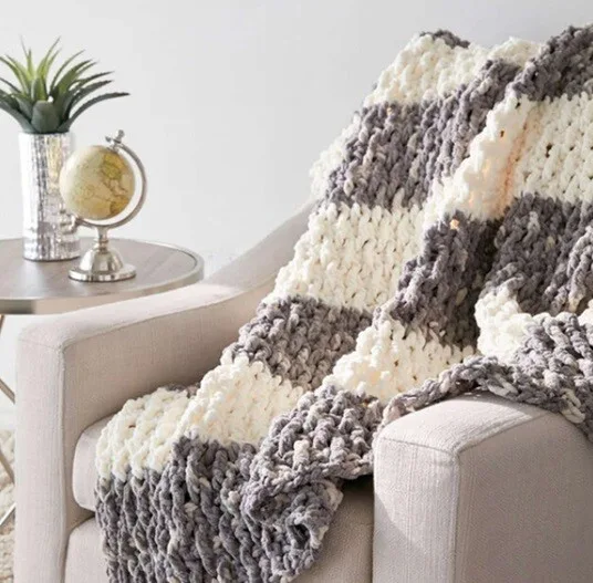 A blanket worked in bulky yarn in stripes of cream and light brown is draped over a chair