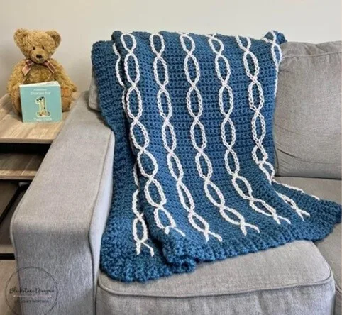A chunky blanket is folded and draped over the back of a sofa