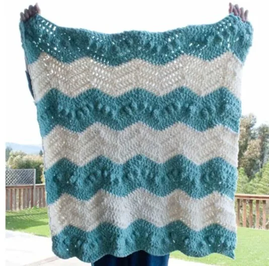A blanket in stripes of white and jade is being held up