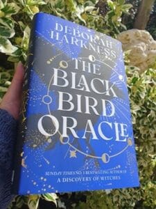 The Blackbird by Deborah Harkness is being held up in front of a laughing gargoyle and greenery