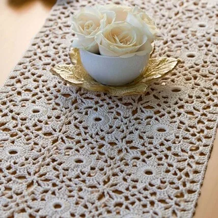 A lacy table runner crocheted in motifs is styled on a table with a pot of roses in the middle of it