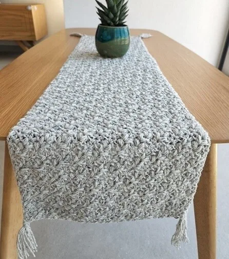A rectangle table is decorated with a boho runner.  A plant sits on the runner