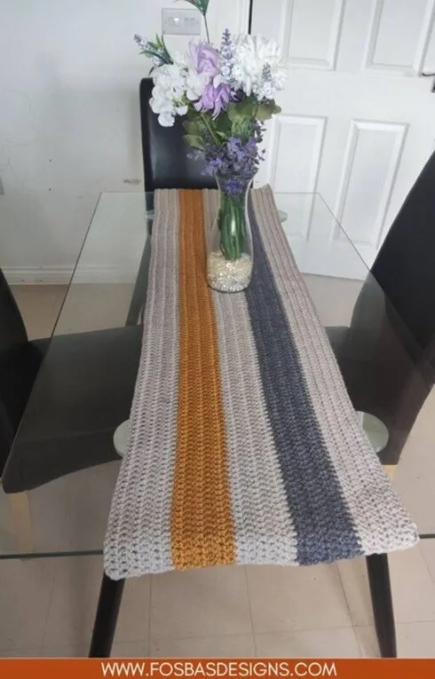 A striped runner is styled on a dining table with a vase of flowers on top of the runner