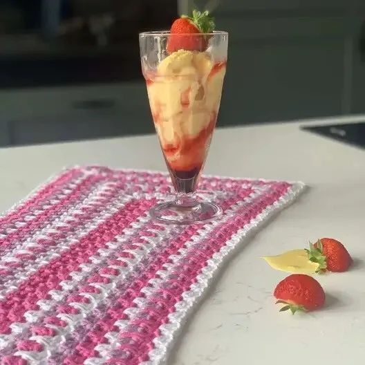 A table runner crocheted in shades of pink is styled on a table with an ice cream sundae on the runner