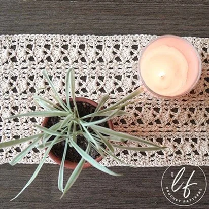 A plant and lit candle are sitting on a lacy table runner to show how the runner protects the surface of the table