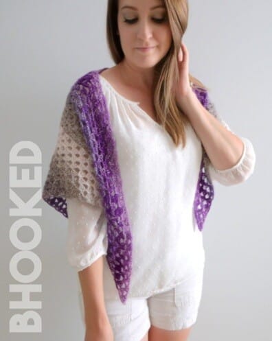 Lightweight crochet shawl in a gradient of gray to deep purple, draped around a woman's shoulders over a white blouse and shorts. The shawl features a lacy, open stitch pattern