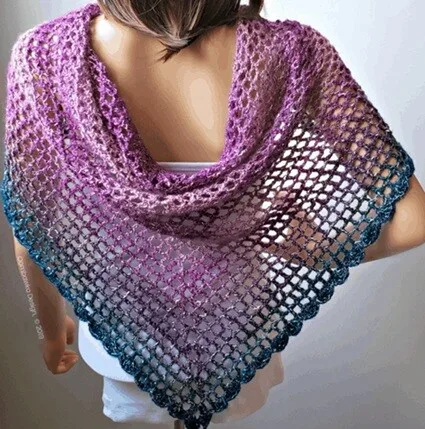 Lightweight crochet shawl in a gradient from plum purple to deep teal, draped over a mannequin’s shoulders with a lacy openwork pattern and scalloped edge. The triangular design highlights the drape and color shift of the yarn.