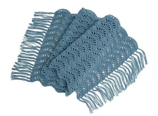 Folded rectangular crochet shawl in dusty blue, featuring a delicate fan stitch pattern and long fringe on both ends. The textured design and soft drape make it a versatile accessory for layering.