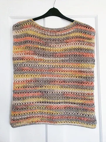 The Orla Crochet Pullover displayed on a hanger without sleeves, showing a sleeveless or vest-style version of the pattern. The lightweight 4ply fabric features pastel stripes and an open stitch pattern. The garment hangs against a white panelled background.