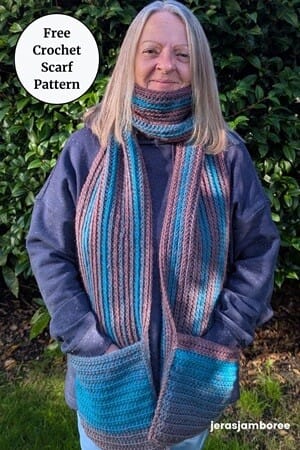 Woman standing outdoors wearing The Glen Scarf, a chunky crochet scarf with teal and mauve ribbed stripes. The scarf has a knit-look crochet texture and deep pockets at each end. Text overlay reads ‘Free Crochet Scarf Pattern