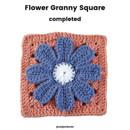 Completed Flower Granny Square showing a white centre surrounded by eight raised blue petals and an orange crochet background. The square forms the floral motif used in the Cosmos Hot Water Bottle Cover.