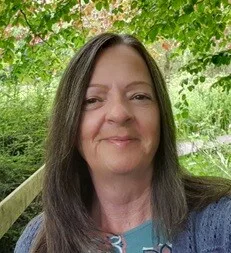 Website owner Sharon Goodwin is standing outside underneath trees