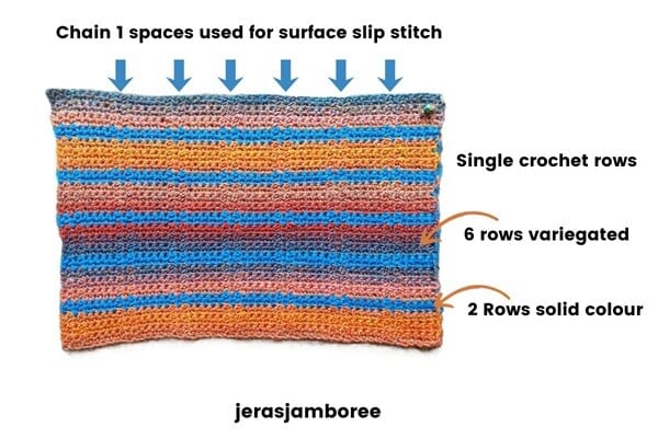 Flat rectangle of the Lennox Crochet Book Cover showing stripe sequence of six variegated rows and two solid colour rows in single crochet, with arrows indicating chain-one spaces used for surface slip stitches.