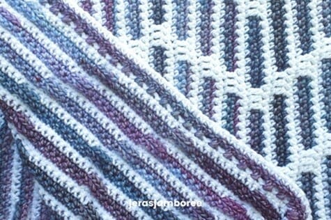 Close-up of the Heather Zig Zag mosaic crochet blanket showing both the front and back sides. The front displays a bold zigzag design in purple and blue on a white background, while the back reveals horizontal striping with the same color palette, highlighting mosaic crochet technique