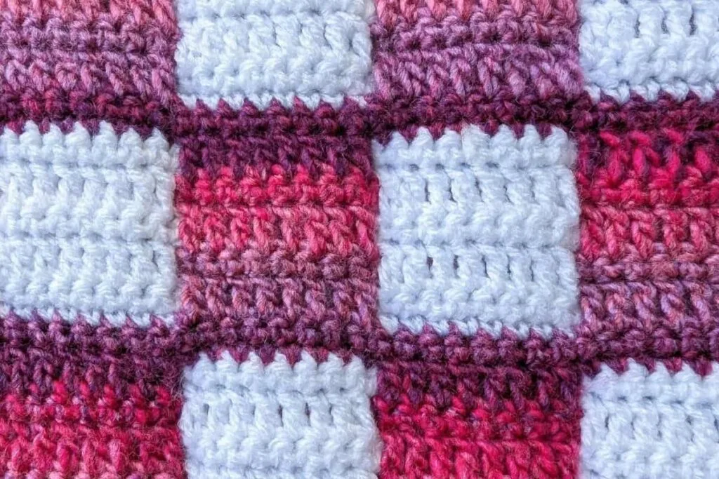 Close-up of the crochet fabric showing the pink and white gingham pattern of the Mindful Hands Mosaic Blanket, highlighting the stitch texture and colour contrast.