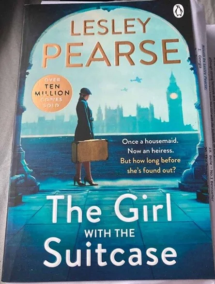 Book cover of The Girl with the Suitcase by Lesley Pearse, showing a woman in 1940s clothing holding a suitcase with the London skyline and Big Ben in the background.