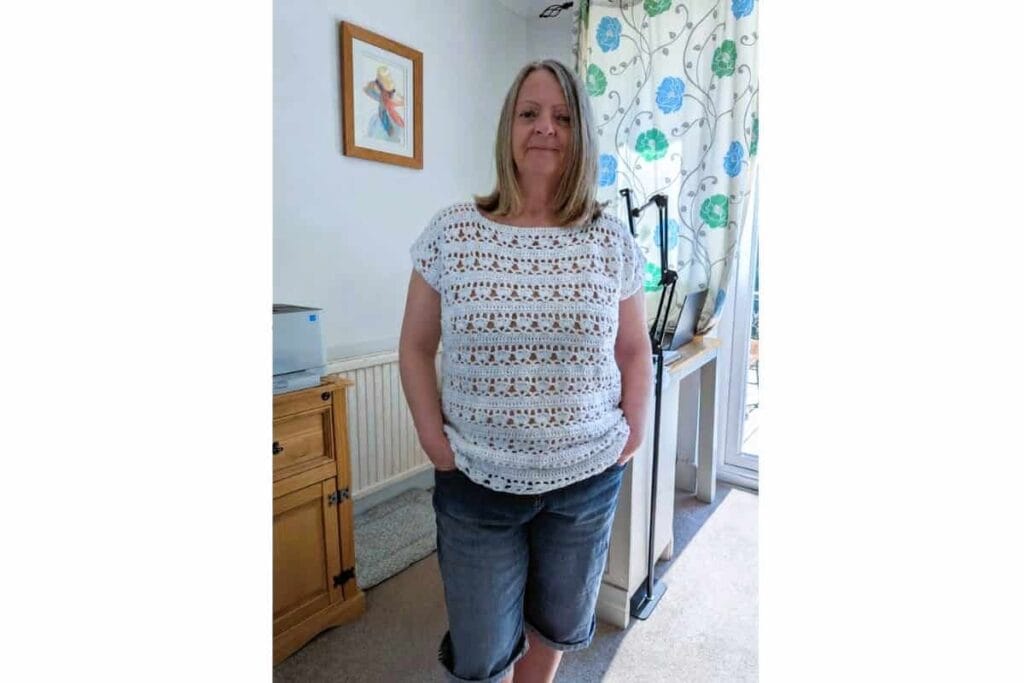 Woman wearing a white crochet summer top with lace stitch detail, styled casually with denim shorts for an easy everyday outfit.
