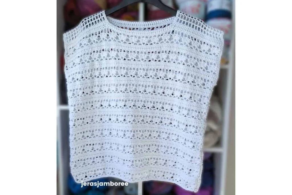 white Lily crochet top hanging on a hanger, showing lace stitch detail and mesh shoulder design.