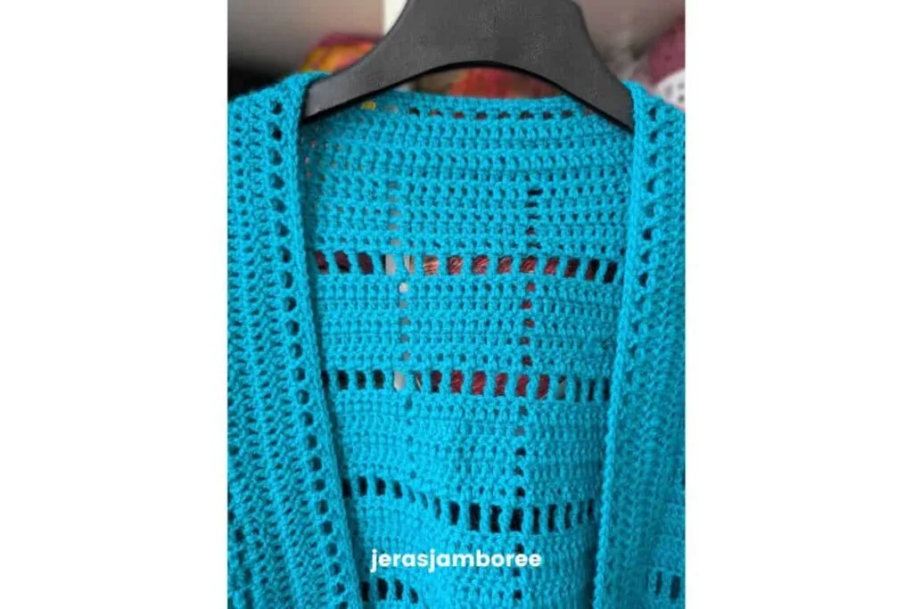 Close-up of the turquoise Marlowe crochet cardigan hanging on a black hanger, showing the back filet square panel and front edging detail.