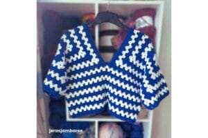 Clover Lane crochet sweater pattern shown in blue and white, hanging in front of shelves of yarn