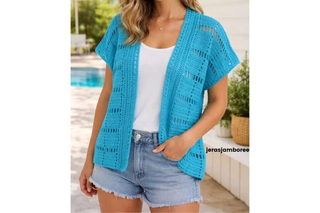 Woman wearing the turquoise Marlowe short sleeve crochet cardigan over a white top and denim shorts in a bright outdoor summer setting.